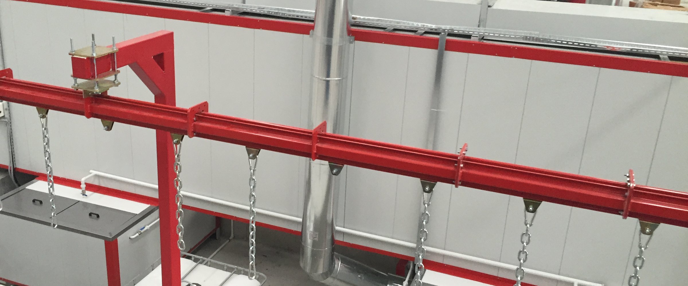 Powder coating plant with spray washing: red cardan conveyor rail, hanger chains and white panelled tunnel